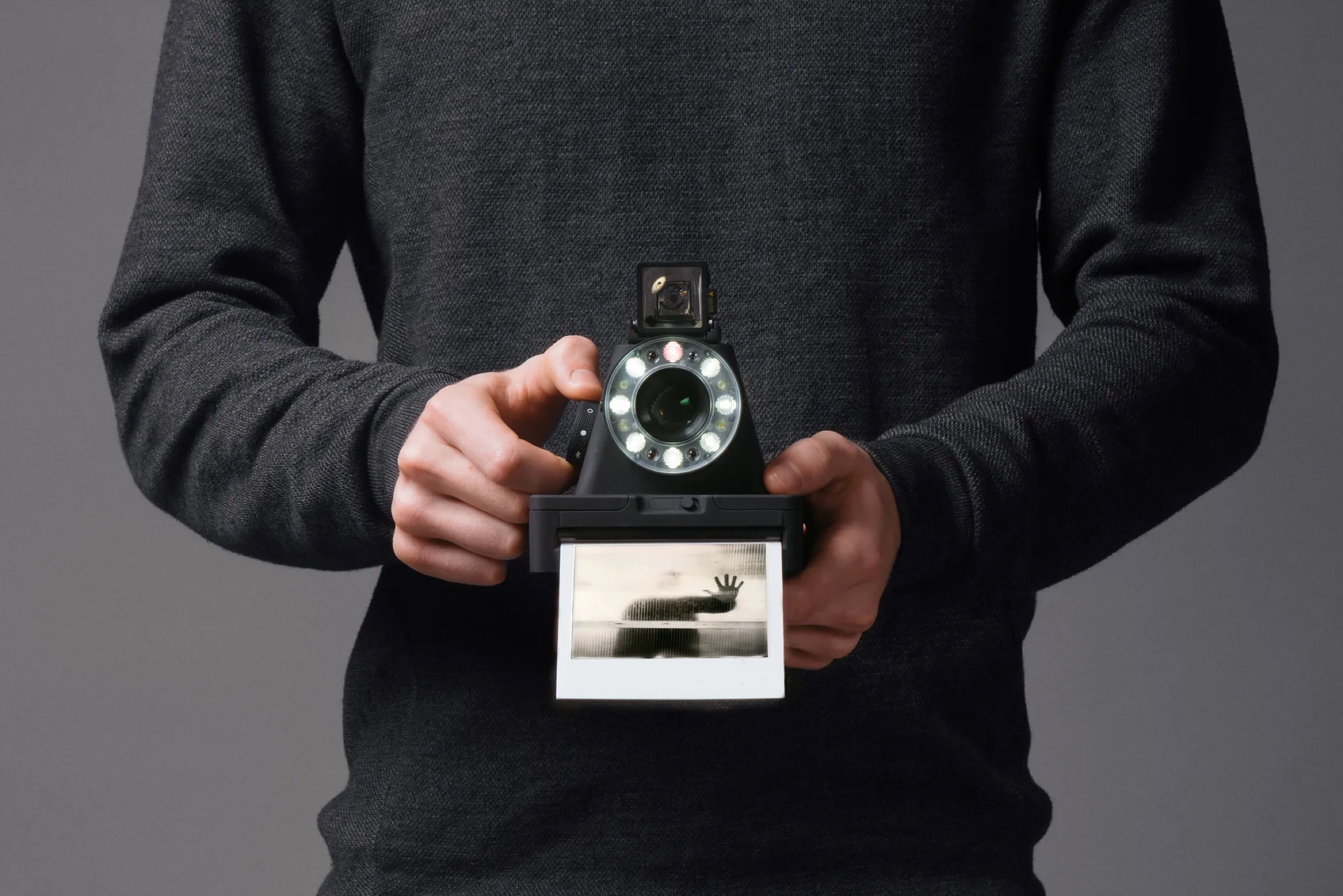 The Polaroid I-1 instant camera held in two hands, with a printed photo coming out